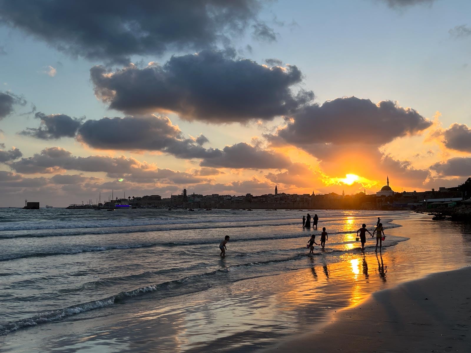 A group of people are playing on the beach at sunset.